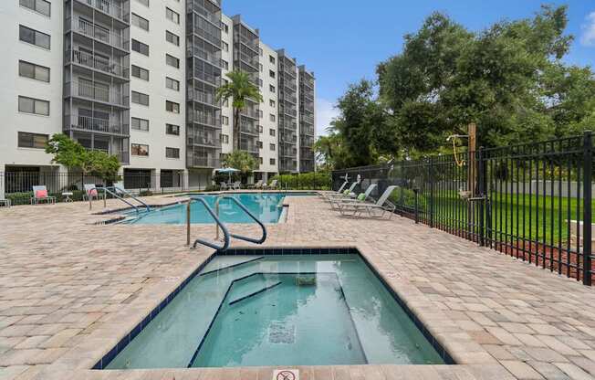 A swimming pool surrounded by a black fence in front of a tall apartment building at Hampton Apartments, Florida