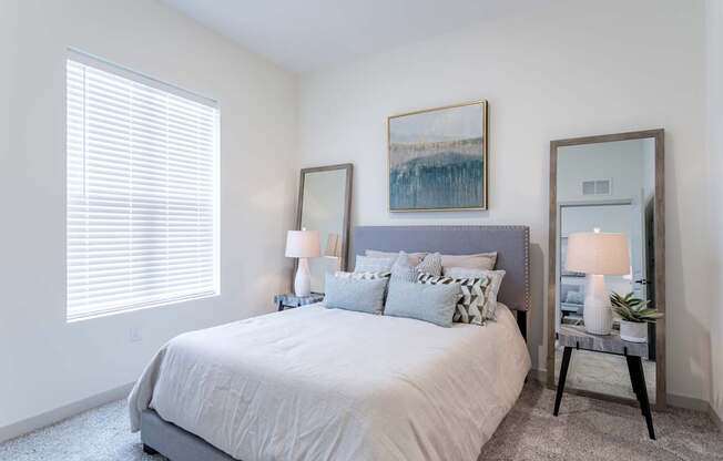 A bedroom with a large bed, two lamps, and a painting on the wall.