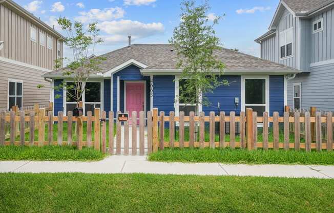 A blue house with a red door and a wooden fence in front.