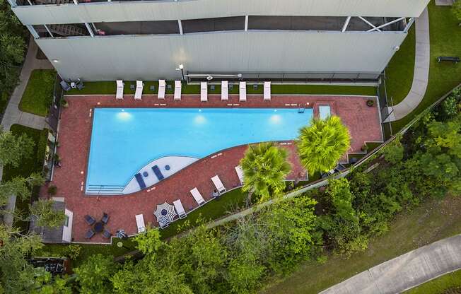 An aerial view of a swimming pool surrounded by trees and a building.
