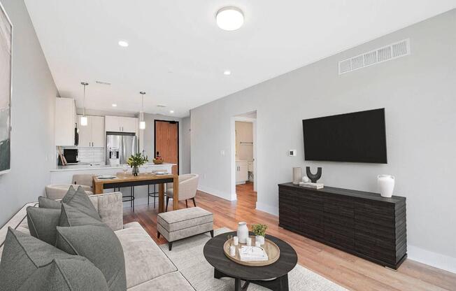 A modern living room with a grey sofa, a wooden coffee table, and a flat-screen TV mounted on the wall.
