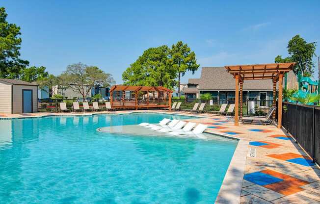 A pool with a wooden pergola and lounge chairs.