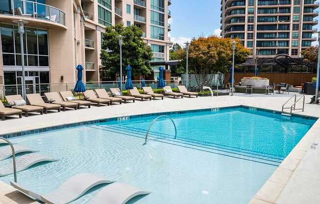 A swimming pool surrounded by lounge chairs and umbrellas in a sunny outdoor setting.