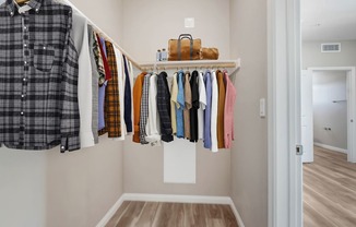 a walk in closet with a rack of clothes and a suitcase on a shelf