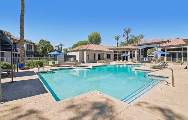 A large swimming pool surrounded by a concrete patio and a few trees.