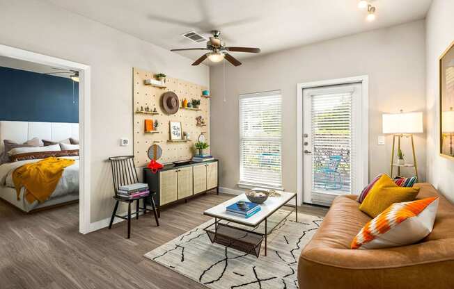 living room area with large couch and natural lighting from porch window/door. ceiling fans and peg board media wall with art and photos. bedroom viewable in background