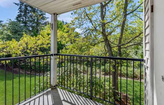 A balcony with a metal railing and a view of a green lawn and trees.