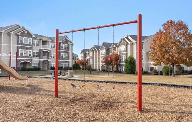 A playground with a red swing set in front of apartment buildings.