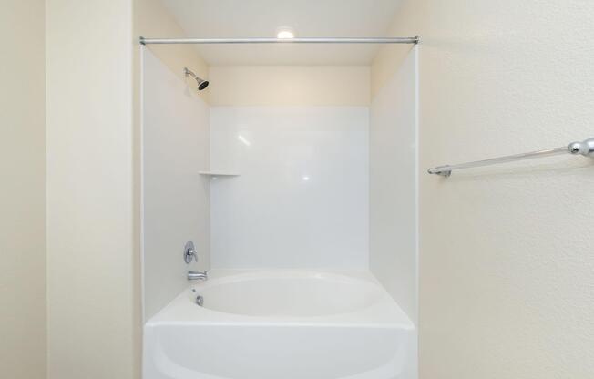 A clean, modern bathroom featuring a white bathtub with a showerhead above. The walls are light-colored, and thereâs a chrome towel bar on the right. The space is well-lit with a ceiling light, creating a simple and inviting atmosphere.