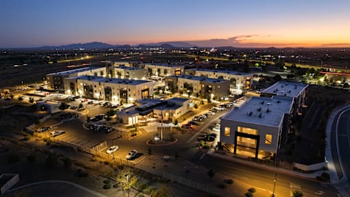 A large building complex is lit up at night with a parking lot in front.