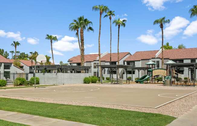 A basketball court surrounded by palm trees and a building in the background.