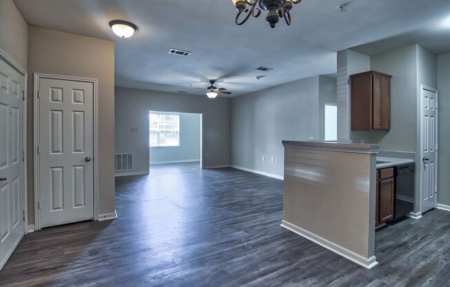 an empty living room with a kitchen and a ceiling fan