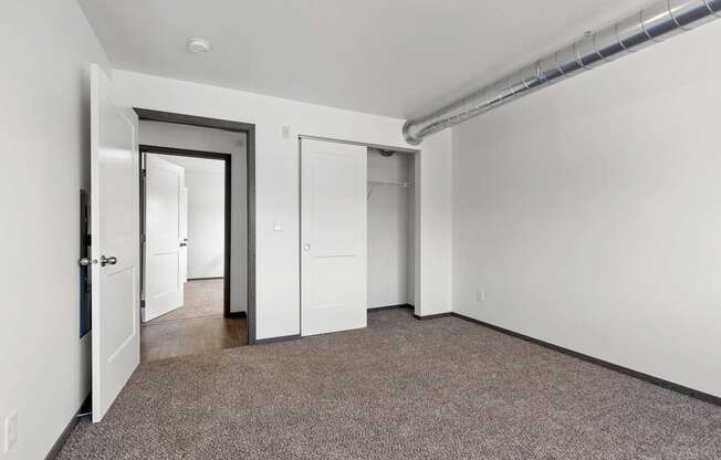 A room with a carpeted floor and white walls, with a door on the left and a window on the right.