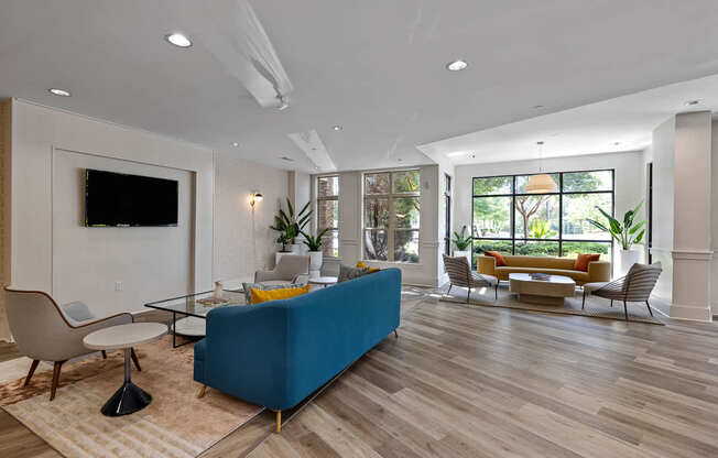 A blue couch sits in a spacious living room with a television mounted on the wall.