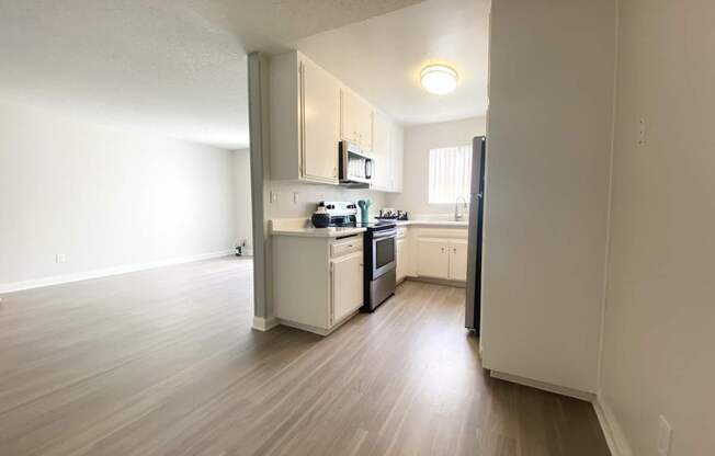 an empty living room and kitchen with wood floors and white cabinets