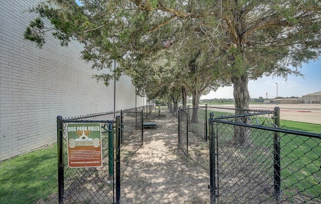 a dog park in front of a brick building with trees and a sign that says dog park