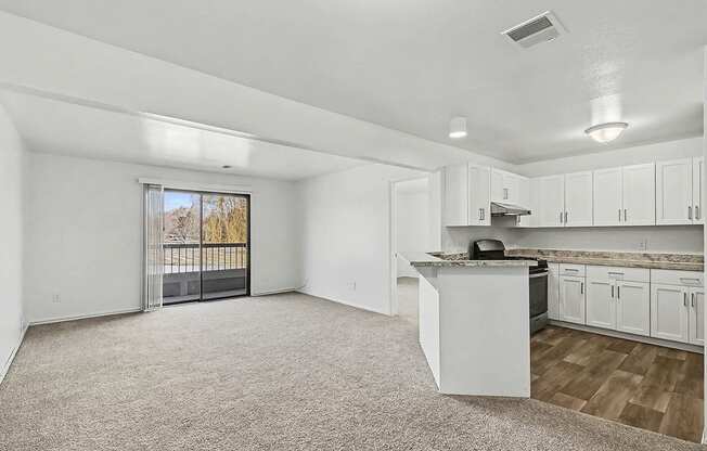 A spacious living room and an upgraded kitchen with white cabinets and a slider to a balcony at Trappers Cove Apartments, Lansing