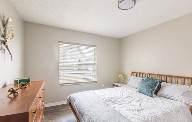 A bedroom with a bed, nightstand, and window with blinds.
