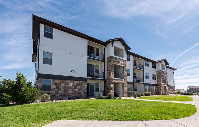 A modern apartment building with a stone facade and a well-maintained lawn in front.