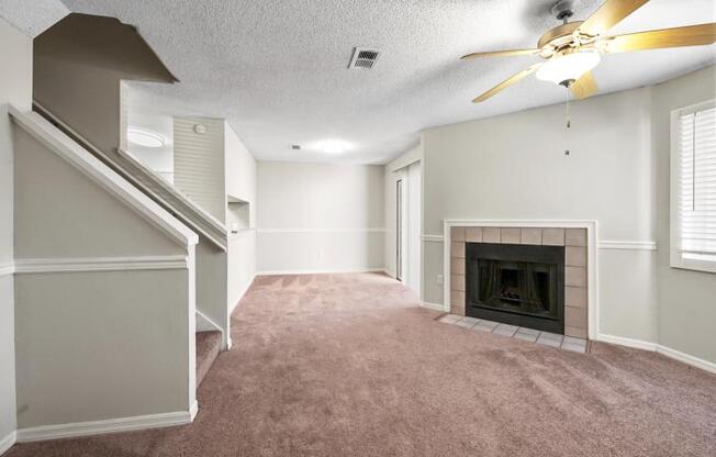 an empty living room with a fireplace and a ceiling fan