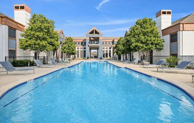 A large swimming pool in front of a building with trees on the side.
