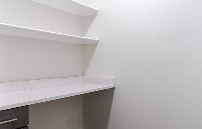 a corner of a room with white walls and a white counter top and a shelf