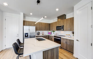 Skye Canyon, NV Apartments Near Las Vegas Strip - Banyan Brighton - Kitchen with Marble Counters, Stainless Steel Appliances, Wood-Inspired Flooring and Cabinets, White Tile Backsplash, and a Large Kitchen Island