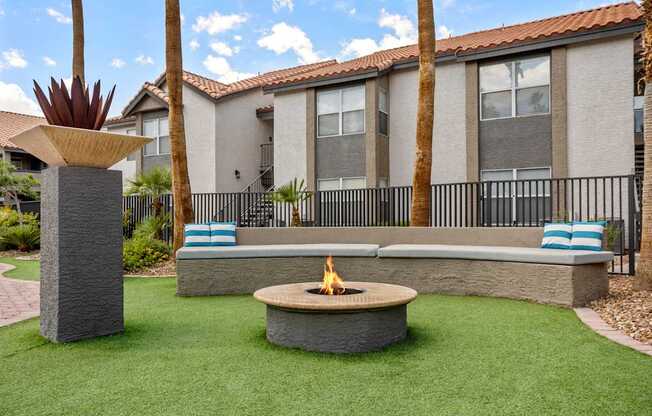 A fire pit sits in the middle of a grassy area in front of a building.