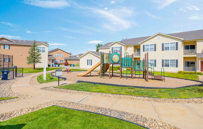 A playground with a slide and swings in front of apartment buildings.