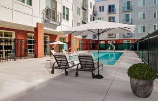 a pool with two lounge chairs and umbrellas in front of an apartment building