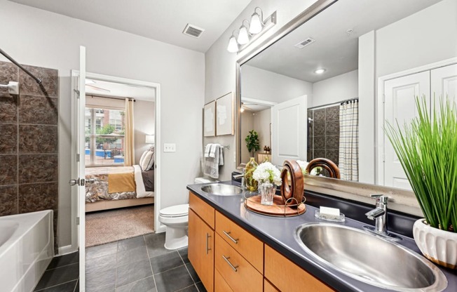 Model apartment master bathroom with a large mirror and a vanity with dual sinks at The Grand at Upper Kirby apartments in Houston, TX