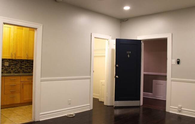 Living room in brookmore apartments in Pasadena featuring dark wood flooring and white wainscoting. Open doorways lead to the kitchen and front closet.