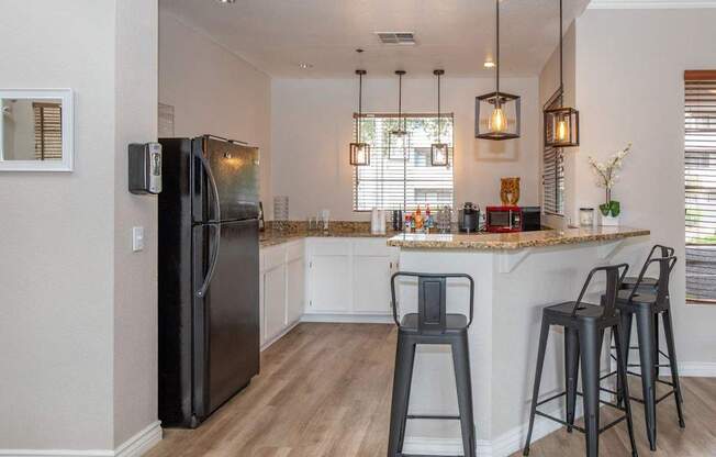 A black refrigerator stands in a kitchen with a bar area.