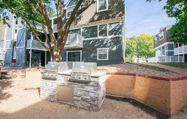 A sandbox with a small building and a tree in front of a grey building.