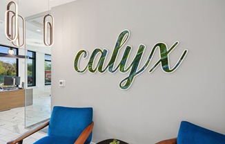 a large neon sign on the wall of a lobby with blue chairs at Link Apartments® Calyx, Chapel Hill