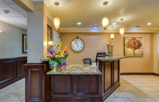 a lobby with a large clock on the wall and a reception desk with a bunch of flowers