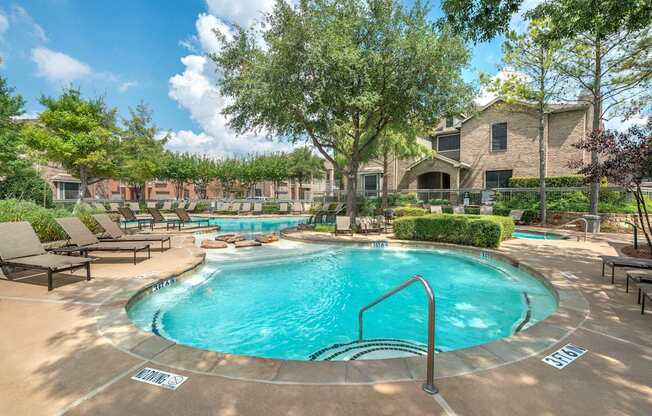 A large outdoor swimming pool surrounded by lounge chairs and trees.
