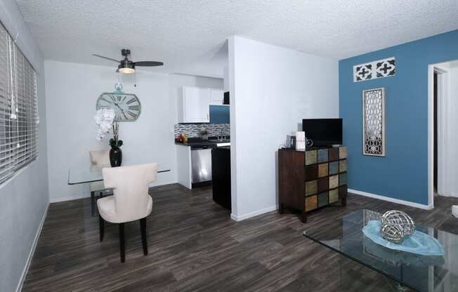 Fifteen 50 apartments Las Vegas open concept dining room and living area with grey wood tile floors and modern glass dining table and cream cloth chairs.