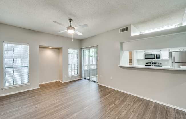 an empty living room with a ceiling fan and a kitchen