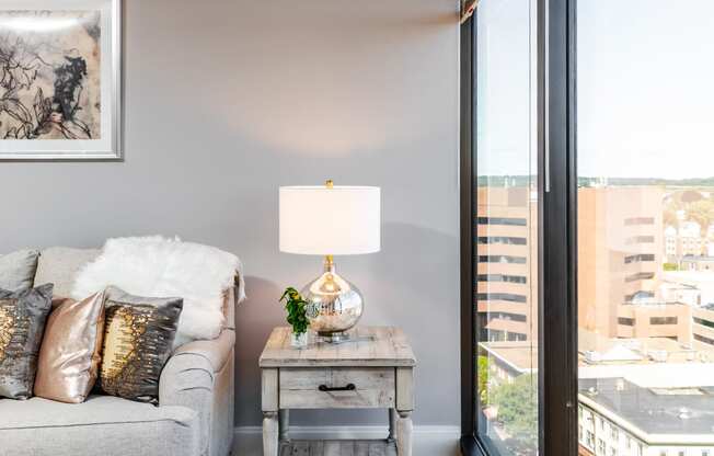 a living room with a gray couch and a table with a lamp and a large window