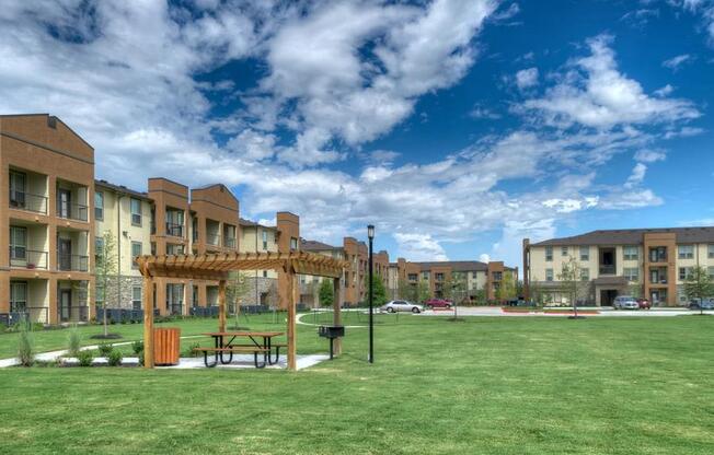 a picnic area in the middle of a grassy area with buildings in the background