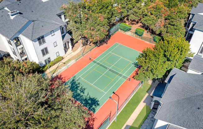 A tennis court surrounded by trees and houses.