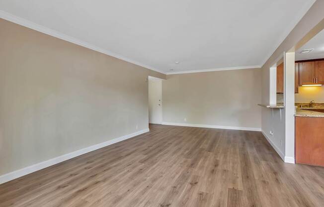 A room with wooden flooring and a kitchen area in the background.