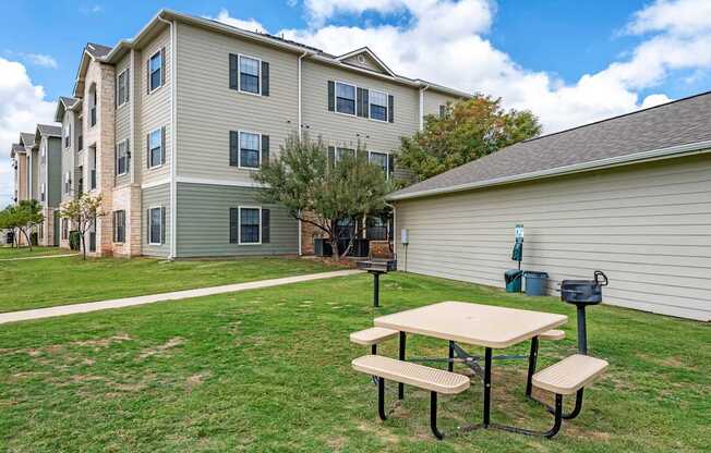 A picnic table is in the foreground of a grassy area in front of a building.
