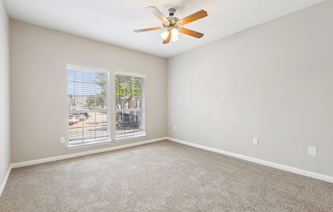 A room with a ceiling fan and a window overlooking a parking lot.