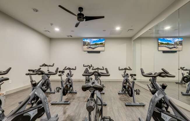 a spacious fitness room with cardio bikes and flat screen tvs