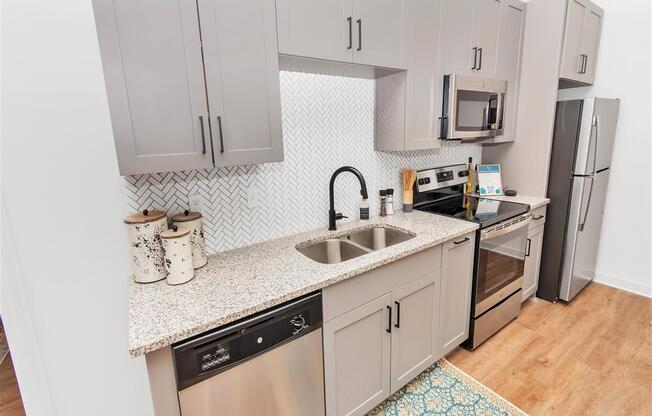 Kitchen with stainless steel appliances, tile backsplash, grey cabinets, and hard floors