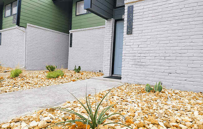 a sidewalk in front of a building with gravel and plants at Ivy Plains at Brooks Apartments, San Antonio