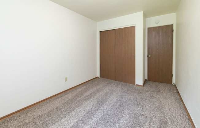 a room with a carpeted floor and a wooden door. Fargo, ND Islander Apartments