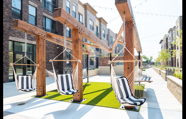 A wooden pergola with hanging chairs is in front of a building.
